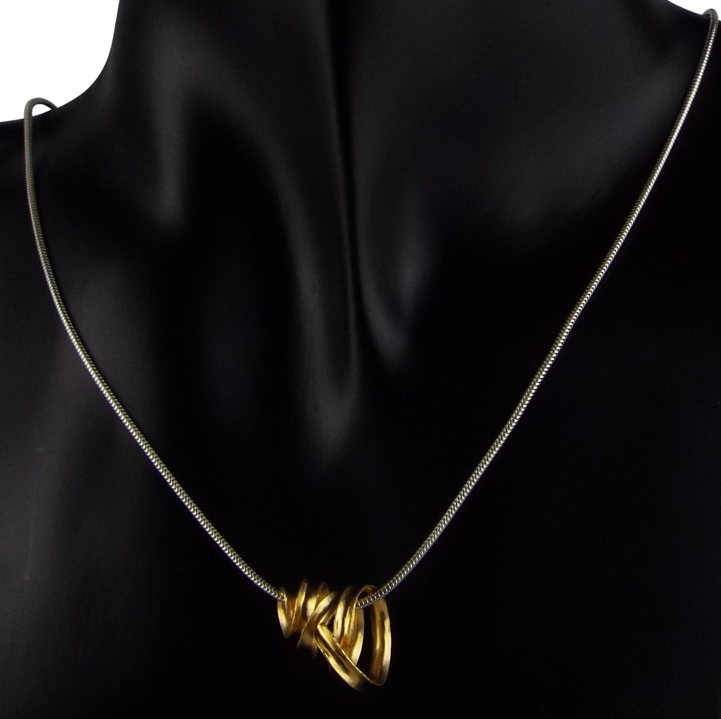 A delicate gold-plated silver ribbon necklace made from a single long strip of sterling silver, formed into a rough spiralling cone, hanging from a silver snake chain. Shown here on a mannequin.