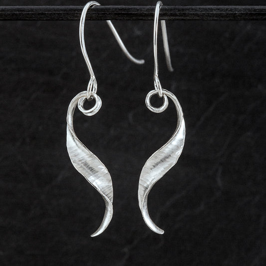 A pair of s-shaped earrings made from recycled sterling silver by the technique of anticlastic raising. The two earrings are mirror images of one another and have a curling, twisting shape. Both are shown here from the front.