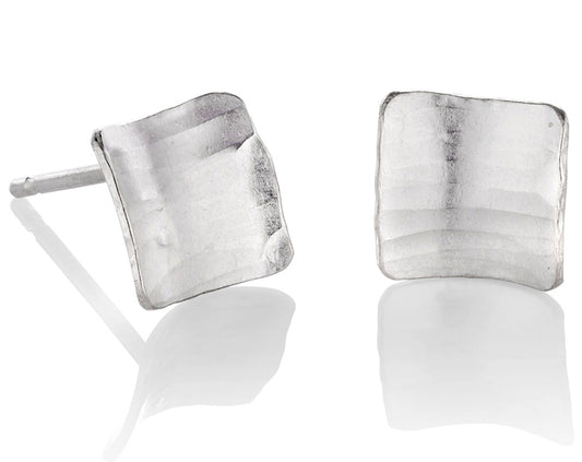 A pair of square silver earrings, studs, with a subtle curve, a hammered texture and burnished edges.