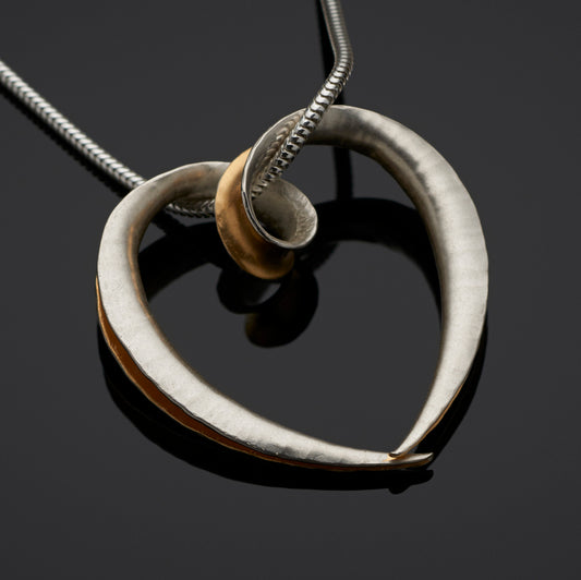 A large silver heart pendant made from a single piece of metal, formed into a sort of tube with the outer side open and gold plated on the inside surface for contrast. It is formed into a loop at the top which the chain passes through.