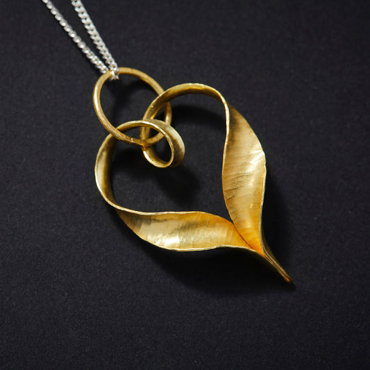 A recycled 18 carat gold heart pendant made from a ribbon of metal, hammered into a continuous heart shape, with a loop at the top for the chain to pass through and elegant twisted ends which join in a point at the bottom.