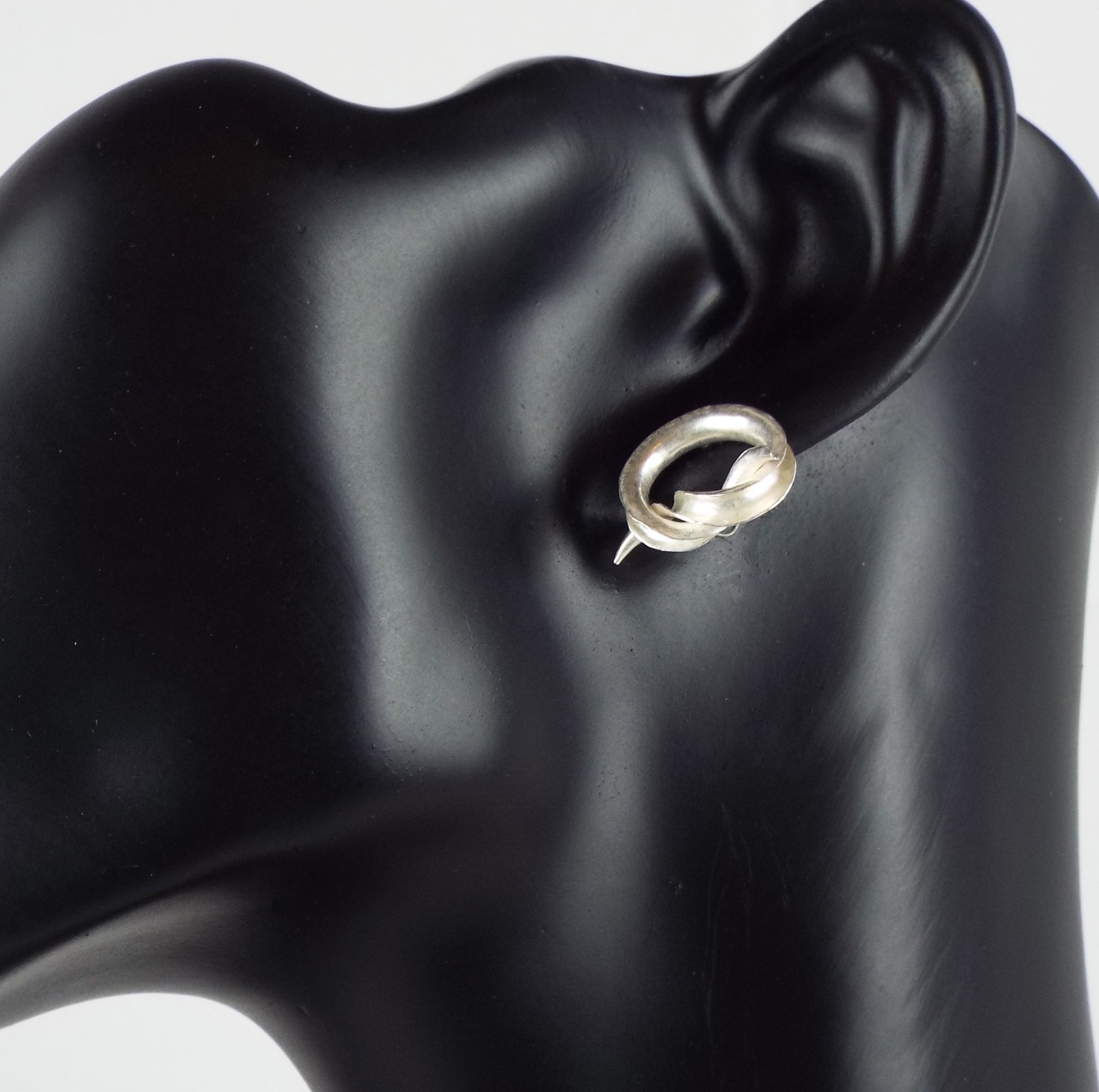 Celebrate tying the knot with a pair of mirror-image stud earrings, each in the form of an open-sided tube tied into a simple knot. Shown on a mannequin.