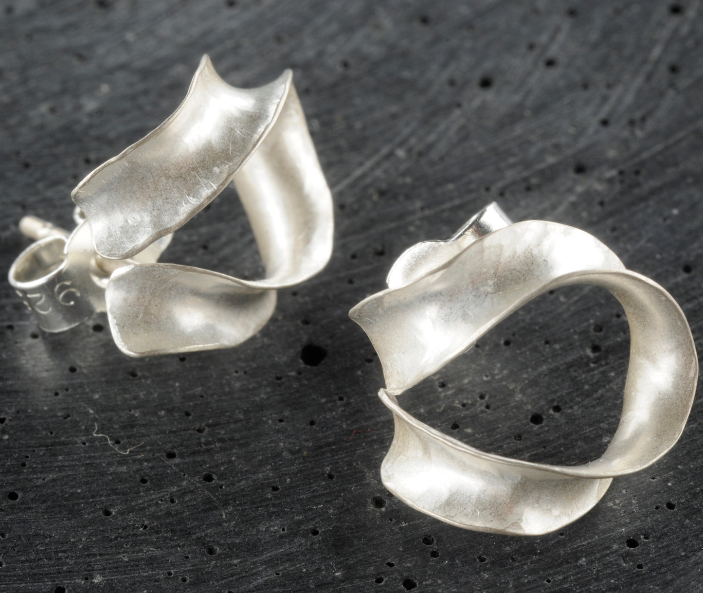 A pair of lightweight silver horseshoe earrings which curl gently below the earlobe. The different views show the three-dimensional curve. They fasten with a silver butterfly.