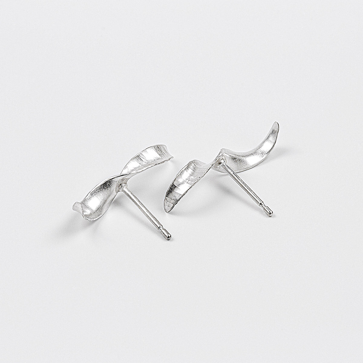 A pair of simple mirror-image silver twist earrings. They each have a stretched-S shape, a hammered texture, non-shiny finish and glittering edges. Shown on a white background, with the two at different angles.