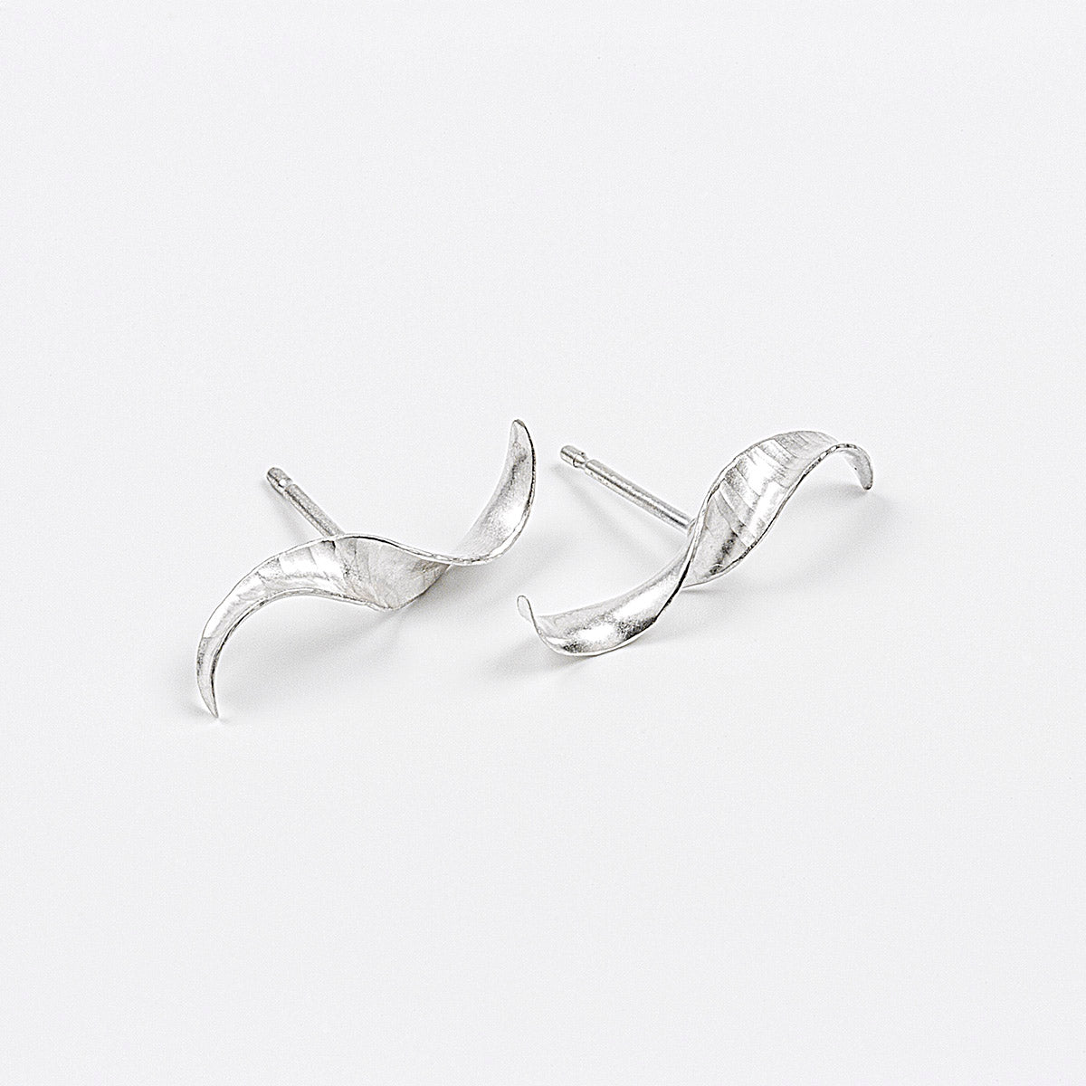 A pair of simple mirror-image silver twist earrings. They each have a stretched-S shape, a hammered texture, non-shiny finish and glittering edges. Shown on a white background, with the two at different angles.