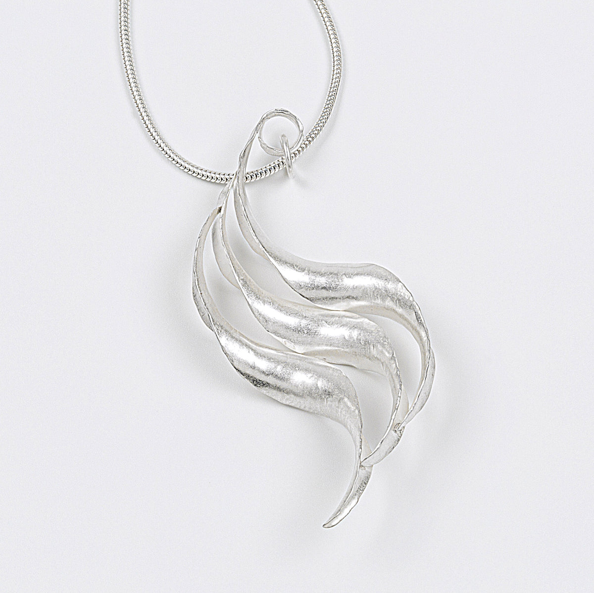 A silver wave necklace, handmade, composed of three curled and twisted units, the top one ending in a loop for the chain. The three units are arranged so that they form a progression. This is a back view.