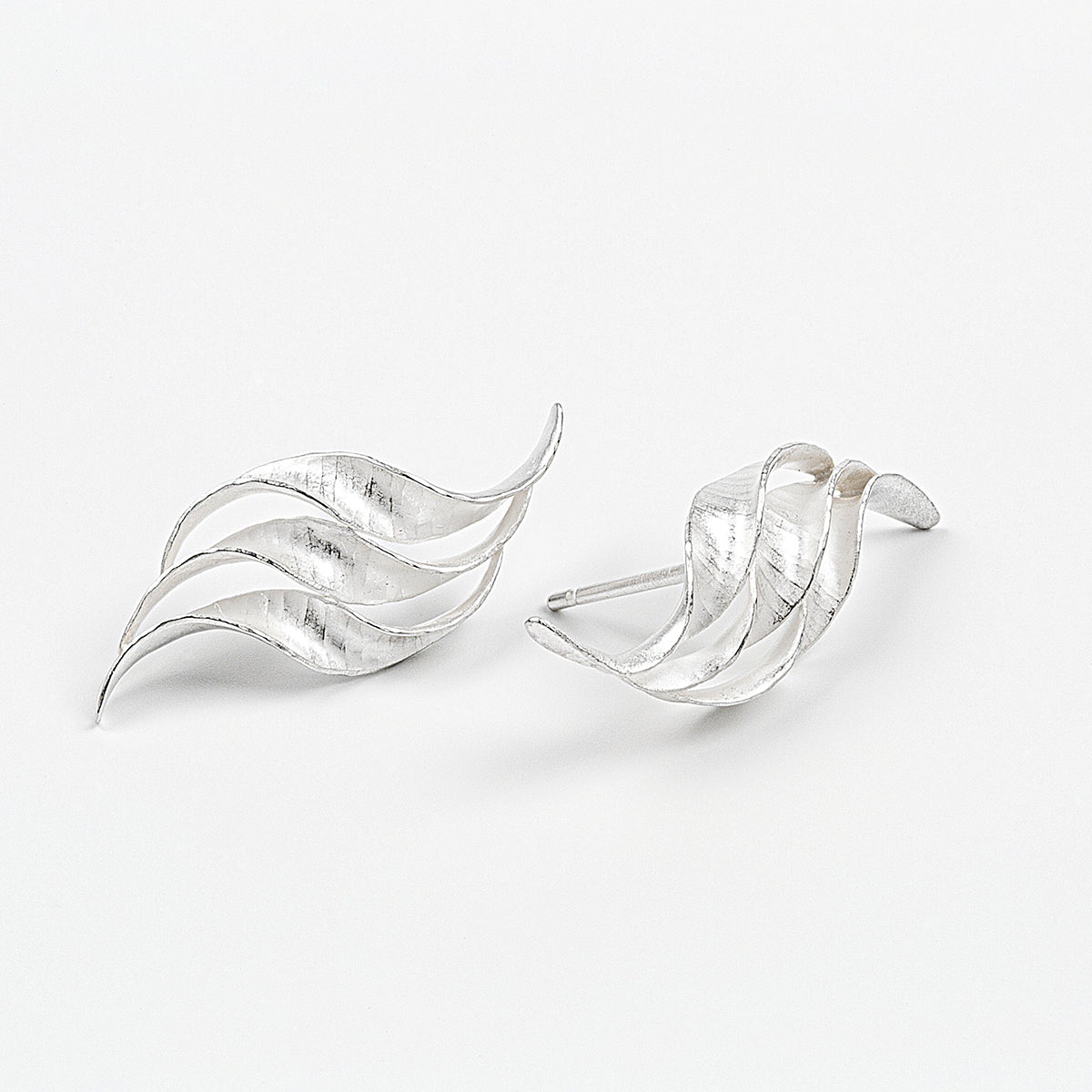 A pair of silver wedding earrings in the form of a triple wave of parallel curling, twisting S-shapes. They have a hammered texture, non-reflective surface and burnished edges.  This image shows one earring from the front and the other from the side.