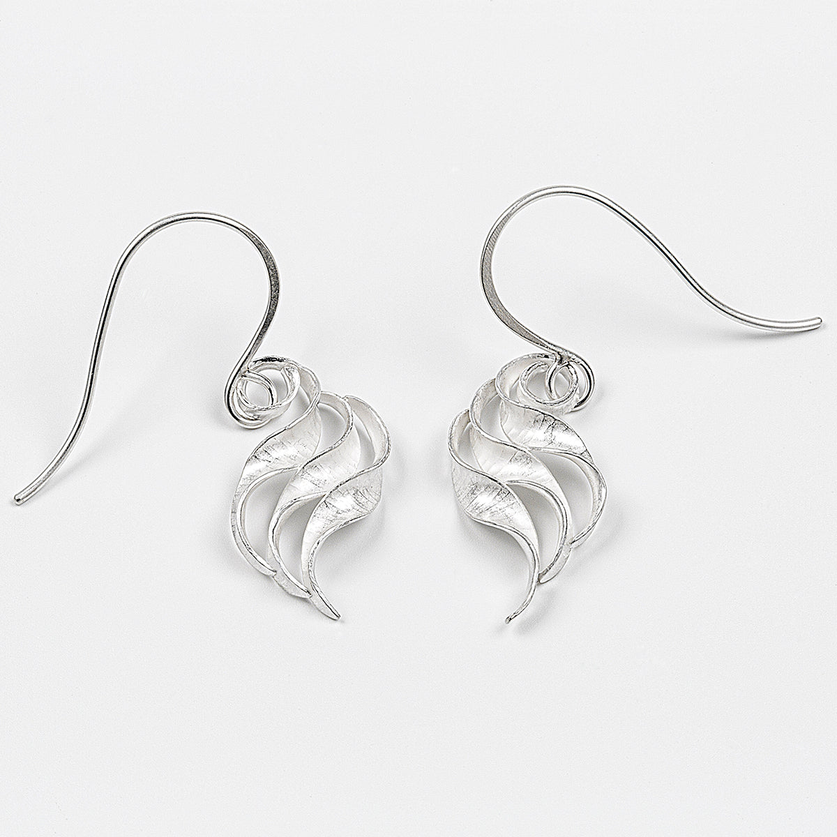 A pair of silver wing earrings made from recycled sterling silver by the process of anticlastic raising. These drop earrings have a hammered texture and non-reflective finish. Each consists of three s-shaped twisted units nested together.  Here a pair of the smaller earrings is shown from the front.