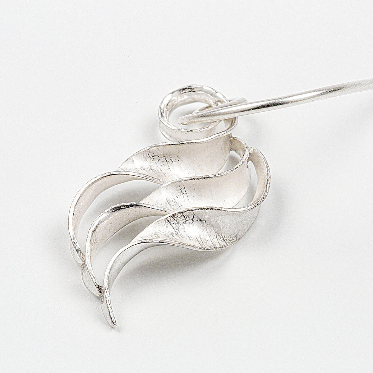 A pair of silver wing earrings made from recycled sterling silver by the process of anticlastic raising. These drop earrings have a hammered texture and non-reflective finish. Each consists of three s-shaped twisted units nested together. This image shows a single small earring.