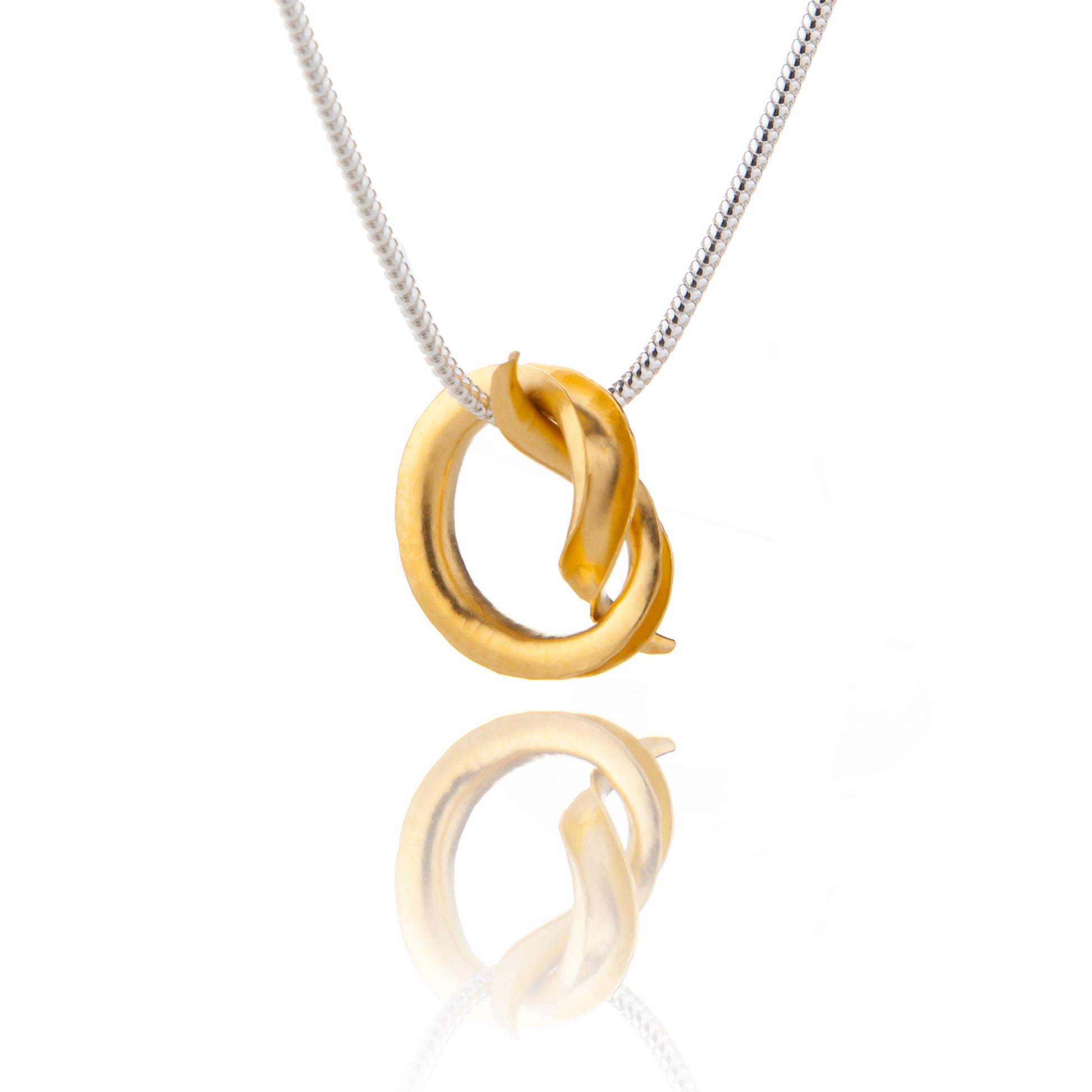 A silver pendant in the shape of a knot, in the form of a tube open down one side and gold plated all over, hanging from a silver snake chain.