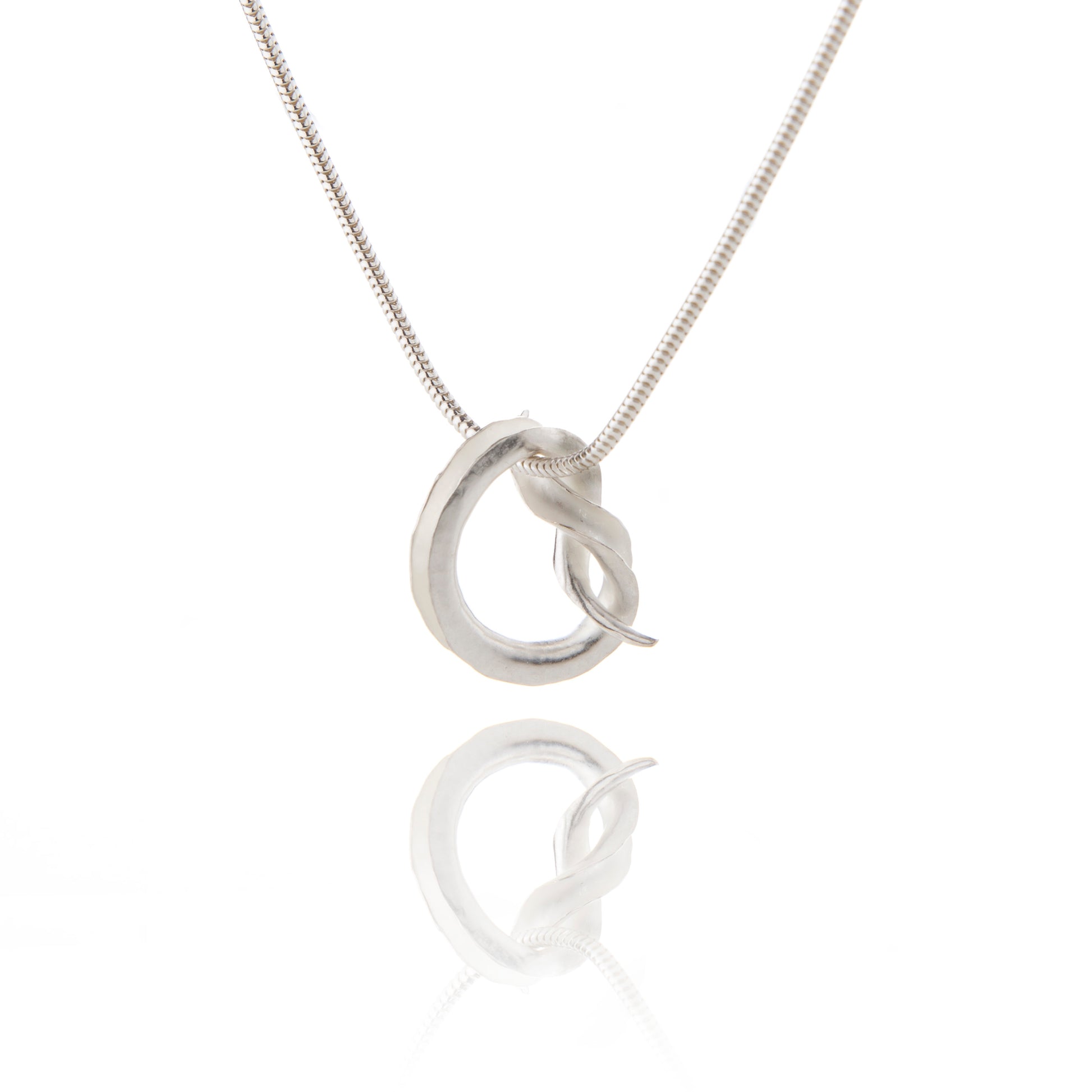 A silver pendant in the shape of a knot, in the form of a tube open down one side, hanging from a silver snake chain.