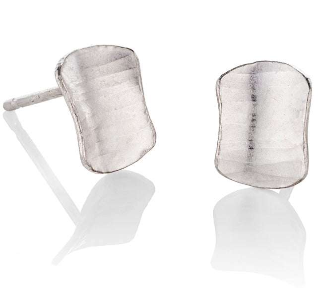 A pair of shield-shaped studs, variations of the square silver earrings, with a subtle curve, a hammered texture and burnished edges.