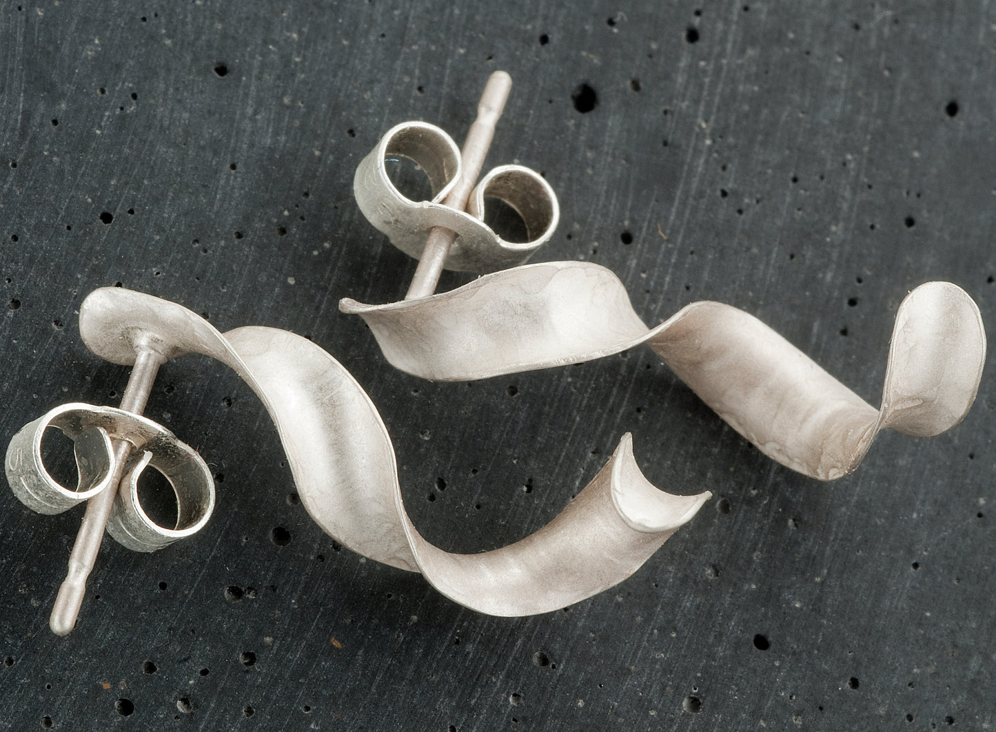 A pair of twisted earrings in sterling silver. They measure about 1.8cm in length. The curly earrings are made by anticlastic raising, which creates simultaneous curves in opposing planes. The finish is satin-matte.