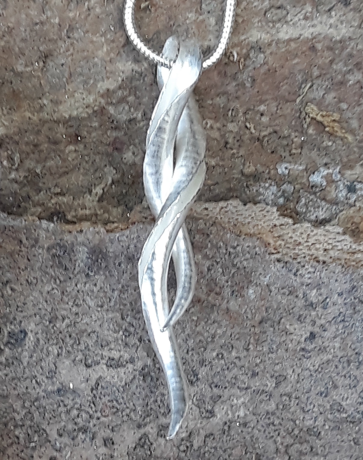 A silver pendant in the form of an open-sided tube, with the two ends twisted around one another, leaving a loop for the snake chain to pass through.