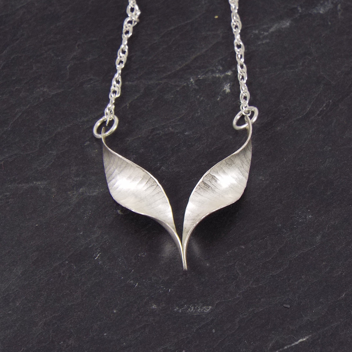 A silver bird necklace made from two mirror-image twisted and curled units soldered at the lower point and attached to a silver rope chain by a silver jump ring at each outer point.