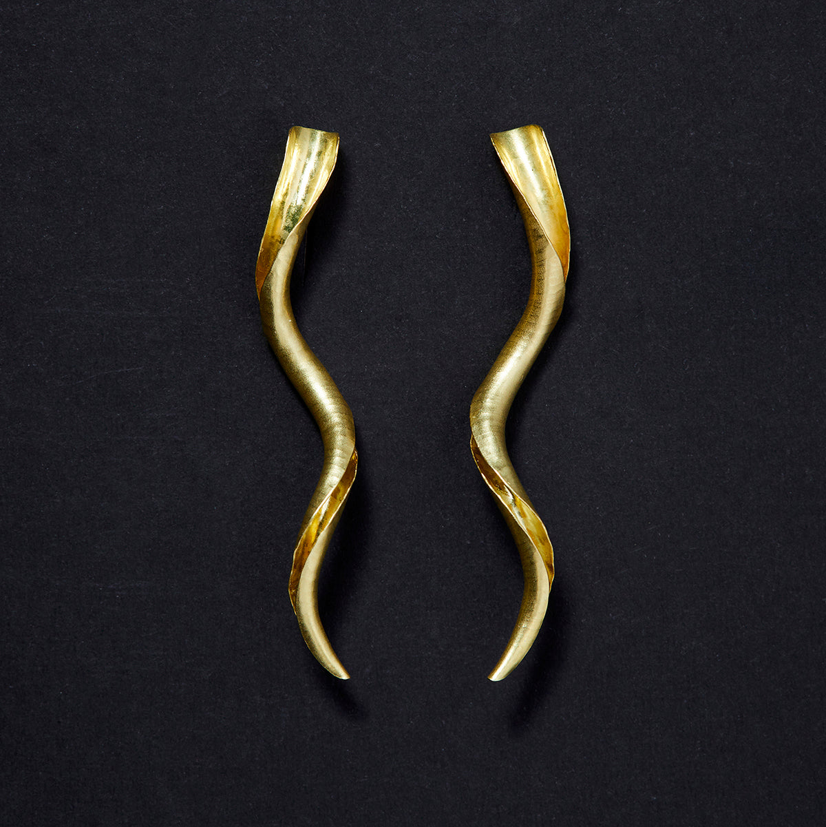 A pair of mirror image gold spiral stud earrings, each in the form of a tapered spiralling tube with one side open to show the inner surface. They have a satin matte finish and hammered texture.