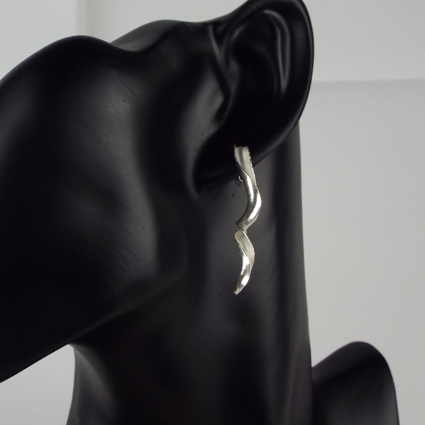 The silver variant of the earrings in wear on a mannequin.