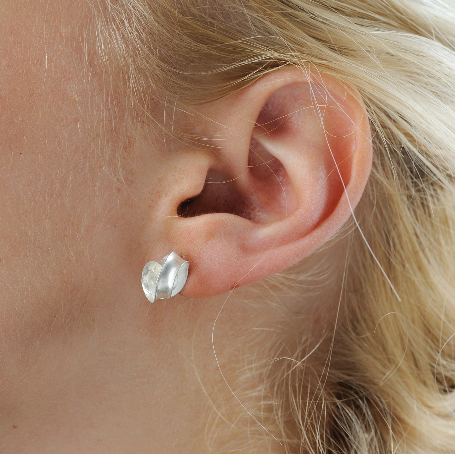 A peir of delicate swirl earrings made from recycled sterling silver. Each stud is made from a single piece of silver, with a spiralloing ribbon of metal twisting so that it lies flat against a curved backing. Shown in wear on a model.