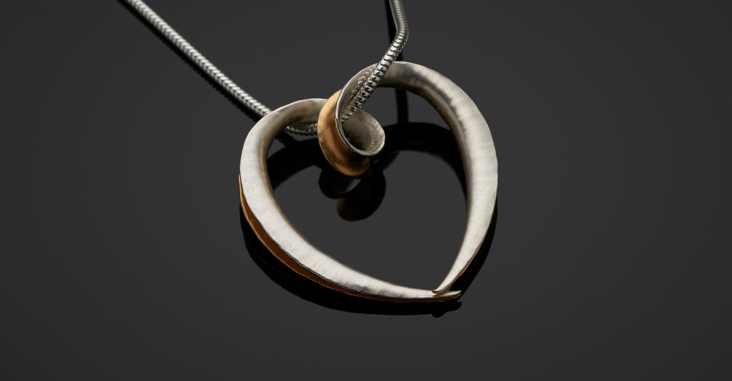 Silver heart pendant in the form of a continuous open tube, with a loop for the chain to pass through and yellow gold plating on the inside surface.