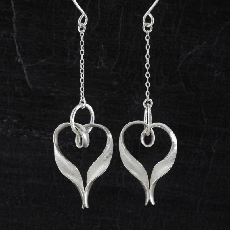 The Ripple silver heart drop earrings in the Chain variant, with a length of delicate silver chain suspending the hearts from the ear wires.