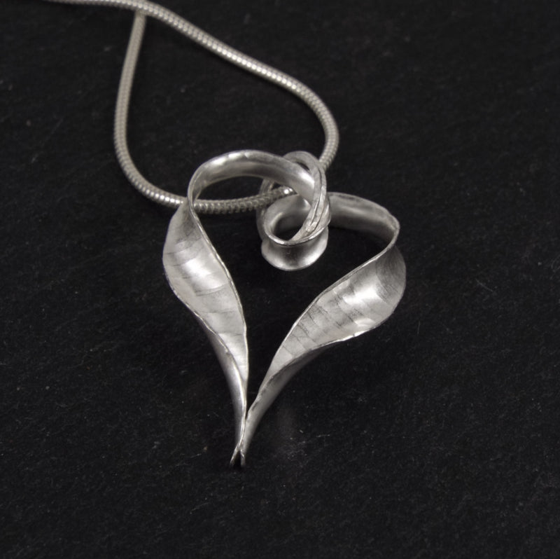 Another view of the Ripple silver heart pendant, from the pointed end, showing the hammered texture and the curling twists above where the ends join.