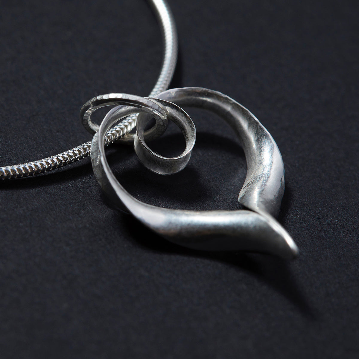 Ripple silver heart pendant on silver snake chain, seen from the back.