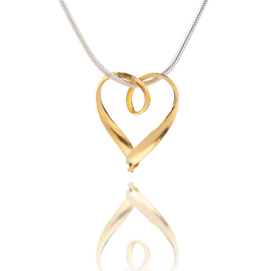 A simple silver heart pendant formed from a continuous strip of recycled silver, thickly plated with yellow gold, hanging from a silver snake chain which passes through a loop in the heart.